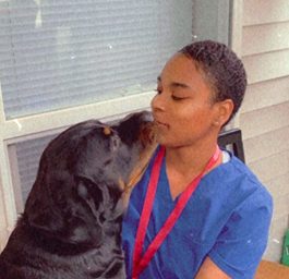 Justice a young adult wearing medical scrubs with a black dog.