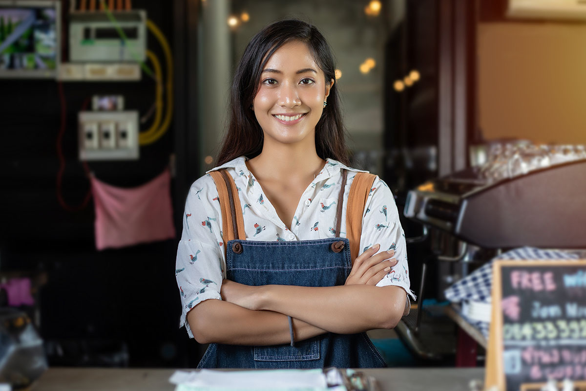 An asian female small business owner stands proudly behind the counter of her business.