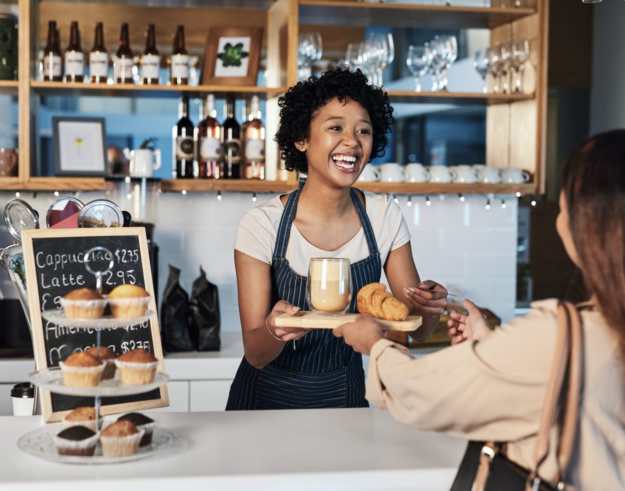 Happy woman, barista and serving customer at cafe for service, payment or order on counter at coffee shop. African person, waitress or employee in small business restaurant helping client at checkout